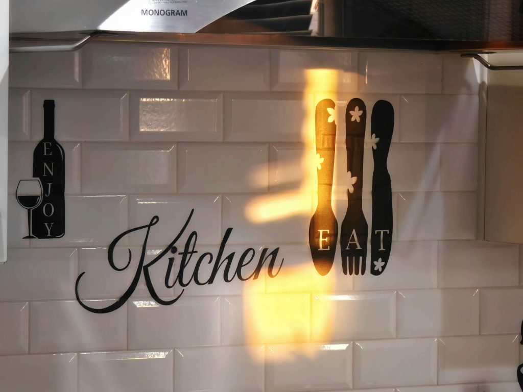 Close-up of a white subway tile backsplash in a kitchen with decorative wall decals and under-cabinet lighting