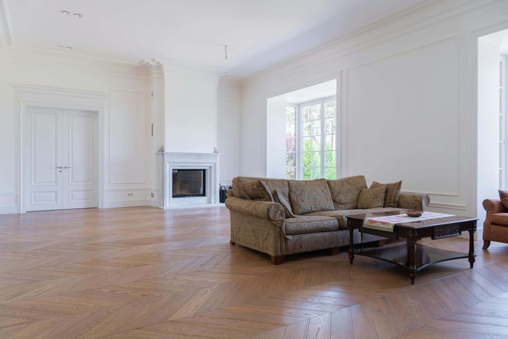 Spacious living room with chevron-pattern hardwood floors, white walls, a fireplace, and classic furniture