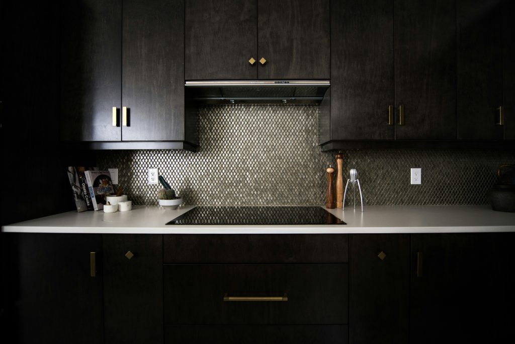 Dark kitchen with metallic diamond mosaic tile backsplash, white quartz countertops, and dark cabinets with gold hardware