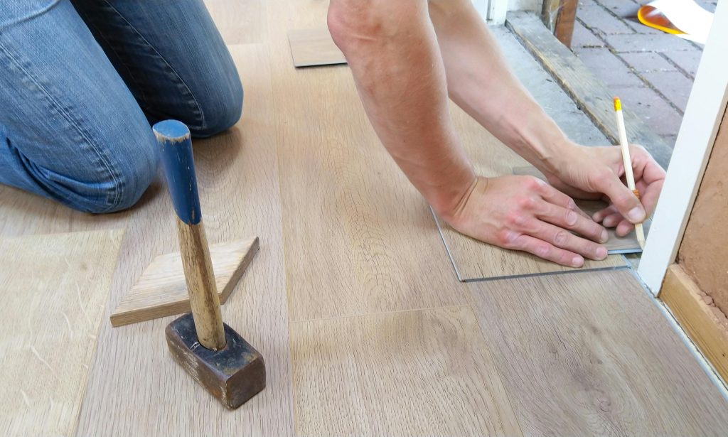 Installer measuring and laying engineered hardwood floor planks with a rubber mallet during installation