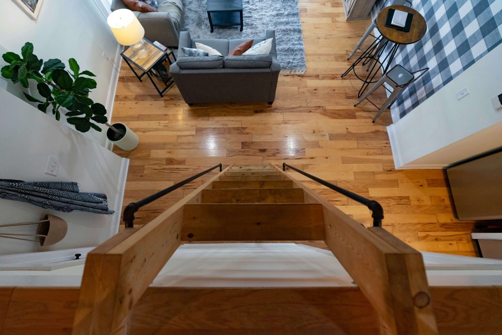 Overhead view of a living room with warm hardwood flooring, modern furniture, and a staircase with black iron railings
