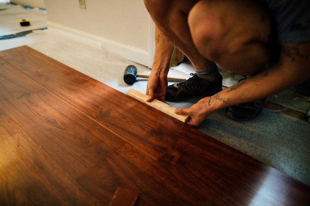 Installer fitting dark hardwood floor planks over underlayment with a rubber mallet during subfloor installation