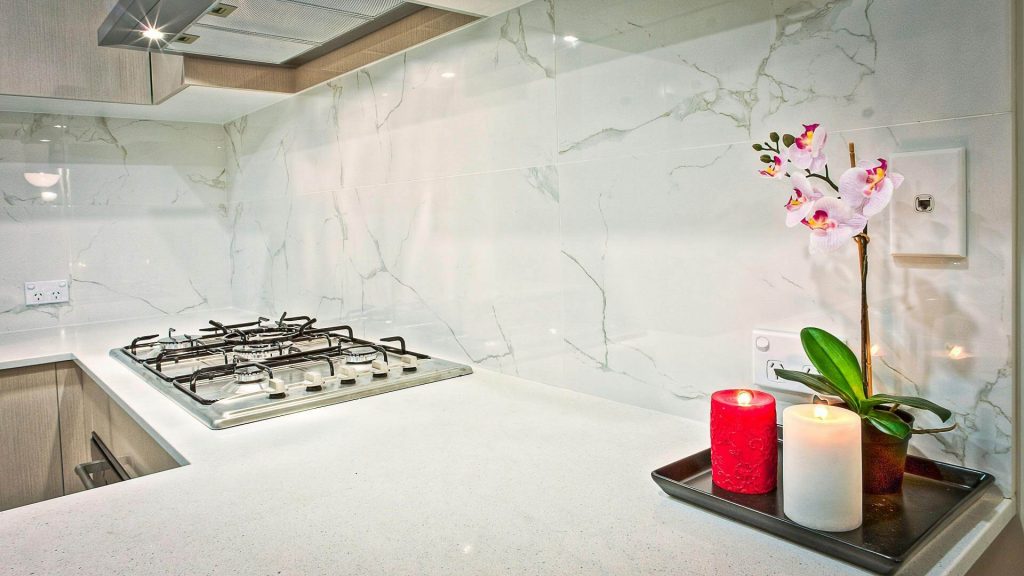 Kitchen with white quartzite slab backsplash, white countertops, gas cooktop, and wood cabinets