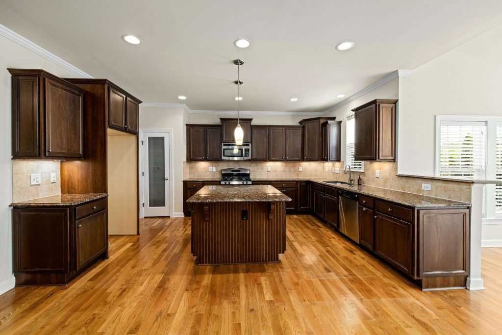 Large kitchen with light hardwood floors, dark wood cabinets, granite countertops, and a center island